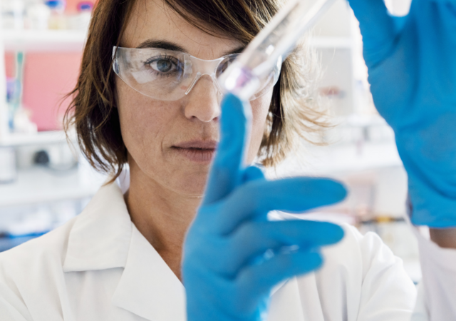 Female scientist in protective gear inspecting a liquid-filled test tube