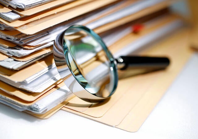Magnifying glass resting on a stack of manila folders and documents