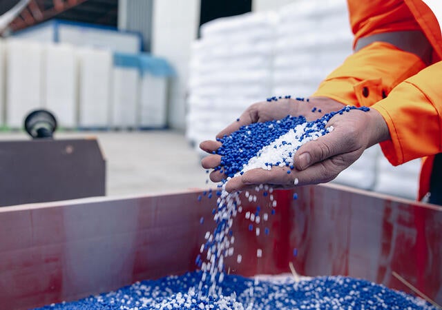 Person in warehouse picking up handfuls of blue and white chemical pellets