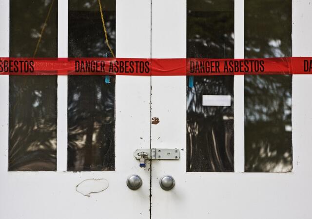 Closed and locked double doors with red tape warning of asbestos 