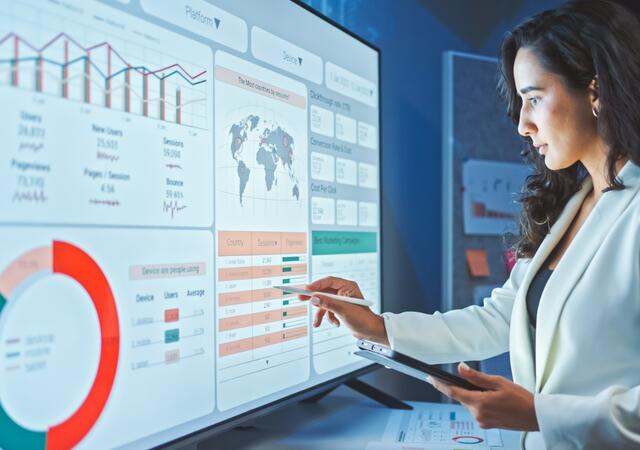 woman in lab coat entering data on large touch screen monitor