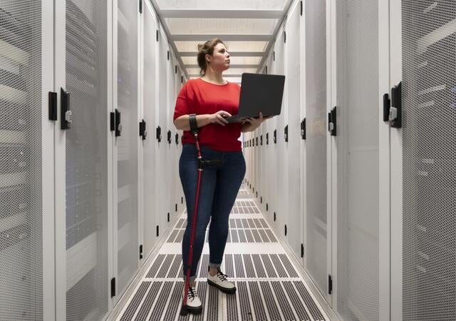 Technician holding a laptop while inspecting a server rack in a data center