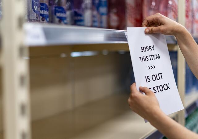 Person hanging a sign on a shelf to notify customers that a product is out of stock