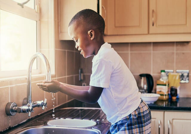 A young child washing hands at a kitchen sink