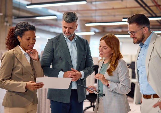 people in office environment all gathered around a woman with a tablet
