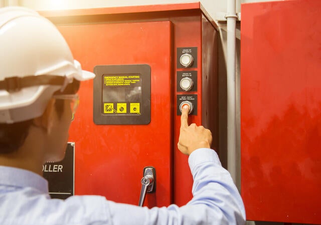 man with hardhat pushing stop button on machine