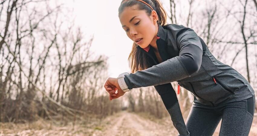 A female runner checks her time on her smart watch. She's wearing black on black performance material workout gear.