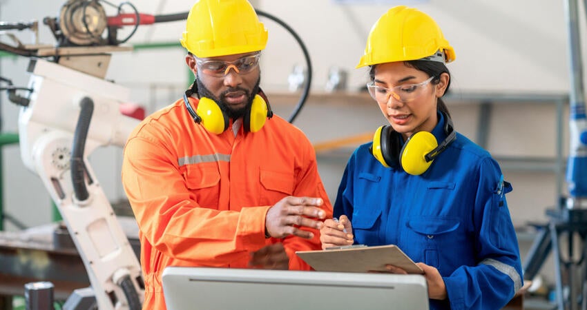 Safety engineer and robot operator talk in front of the production line in a factory.