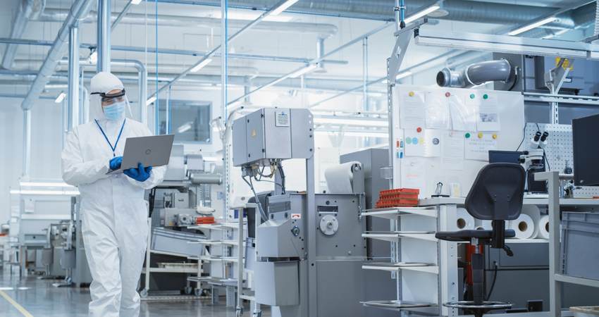 Person wearing PPE and walking through a lab while looking at a laptop