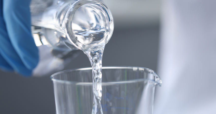 Scientist chemist in gloves pouring water from flask into glass closeup.