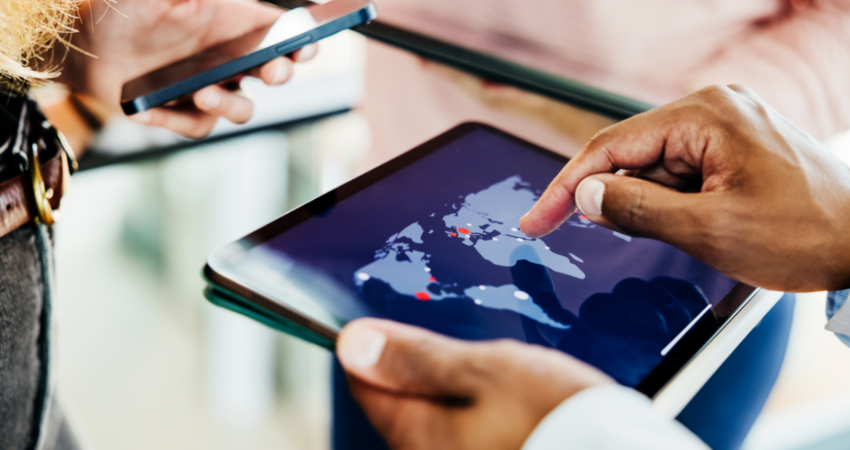 Business professionals collaborate using a digital tablet displaying a global map, indicating international reach and strategic planning