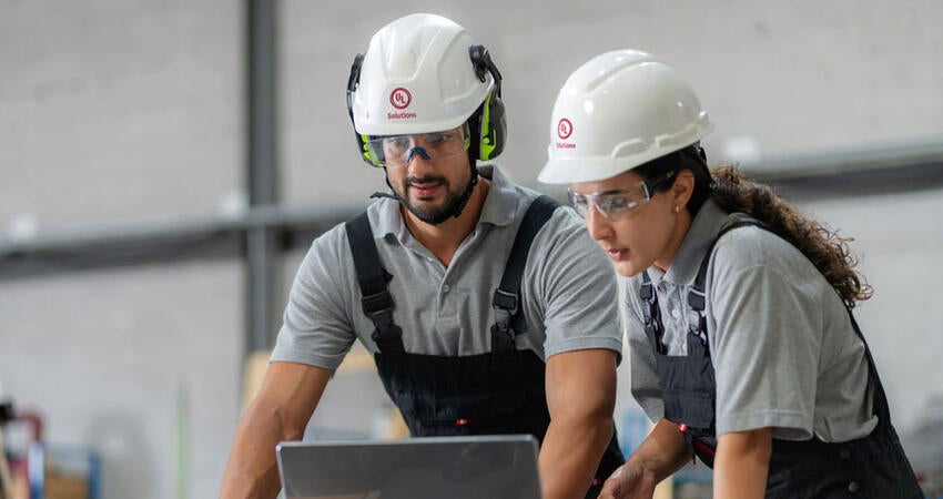 Two people in hard hats working together on a laptop