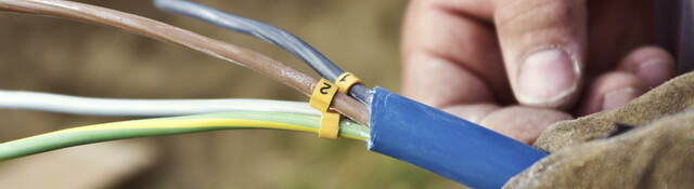 A close-up of a man’s hand holding a cable with exposed wiring. 