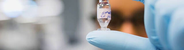 Gloved hand holding a chemical vial in a laboratory setting