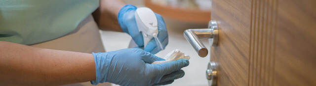 Employee spraying disinfectant on cloth to sanitize door handle