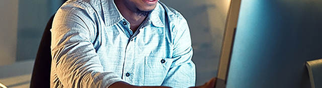 Smiling man sitting at a desk in front of a computer monitor