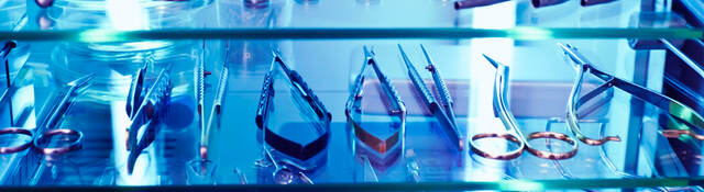 Medical tools sit on a shelf under the blue glow of ultraviolet light, used as a germicidal disinfectant.