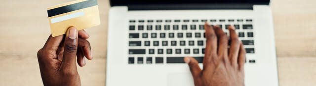 man looking at a credit card and typing on laptop keyboard