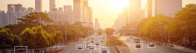 Cars highlighted by artificial intelligence driving down highway with high-rise buildings in the distance