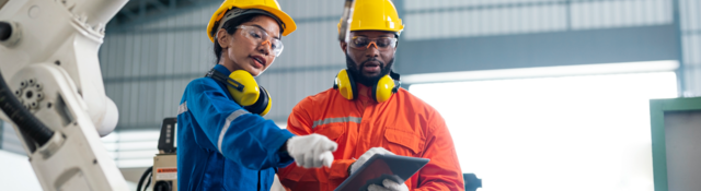 Engineers talking in a factory, with robotic arm in foreground