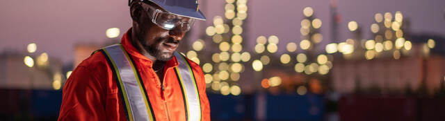 Engineer using tablet near an oil refinery at night