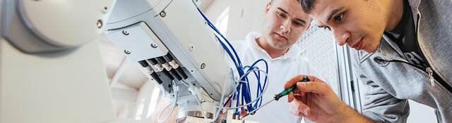 Two techs fine tuning a robotic arm