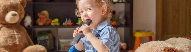 Toddler sitting while chewing on a tv remote