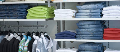 Retail store shelves filled with neatly folded clothes arranged by color. 