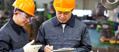 Two men in hard hats writing on a clipboard