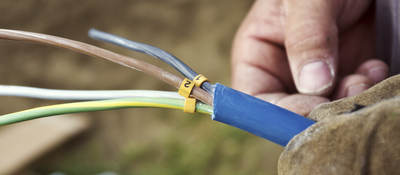 A close-up of a man’s hand holding a cable with exposed wiring. 