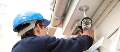 Man in hard hat on a ladder installing an outdoor security camera