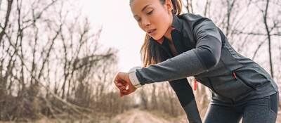 A female runner checks her time on her smart watch. She's wearing black on black performance material workout gear.