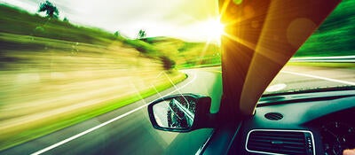 View out of a car on a road with sunlight by left side of the windshield
