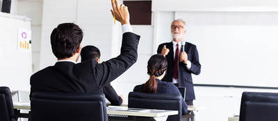 Business man raising hand in a classroom setting