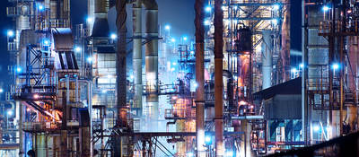 A brightly lit commercial oil refinery is shown at night.