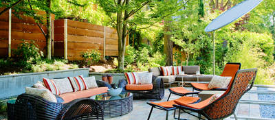 Outdoor furniture including sofa, chairs, table and umbrella in a sunny patio setting