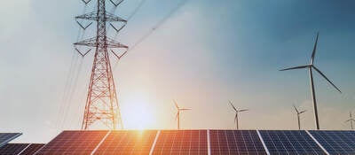 Large electric line tower over solar panels with sun in the background