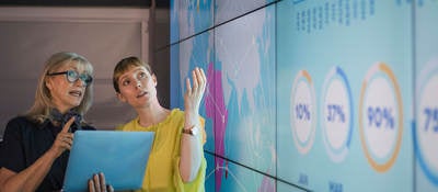 Professionals review data on a laptop and on a larger wall display