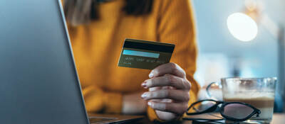 woman holding a credit card and sitting in front of a laptop computer