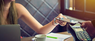 woman tapping a mobile phone for payment in cafe