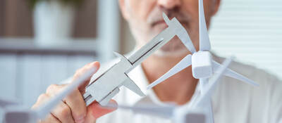 Person measuring a scale model of a wind turbine with calipers