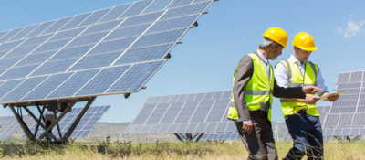 Workers reviewing an engineering report, with solar panels behind them