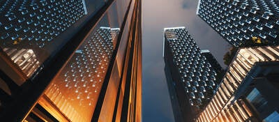 Low angle view of modern skyscraper buildings illuminated at night reflecting on a glass facade 