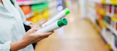 Person comparing green and white plastic bottles in a supermarket