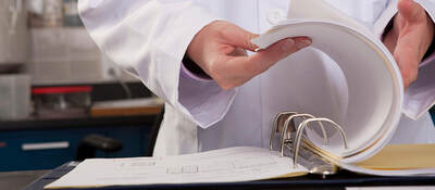 A close up of a lab worker’s hand flipping through three-ring lab binder