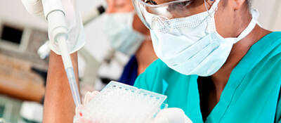 A lab worker in safety glasses and mask using large syringe to fill multicompartment test receptacle