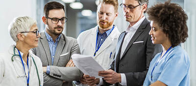 A group of five work co-workers review professional document in a medical setting