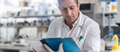 A laboratory worker sitting at a table reviews a guide