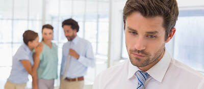 An employee in the foreground noticeably emotional while three coworkers whisper in the background