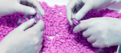 Two sets of hands in latex gloves remove purple pills from foil-backed medicinal packaging